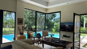 Uma sala de estar espaçosa com uma grande janela com vista para uma piscina, uma televisão de tela plana e um espaço de estar confortável.
