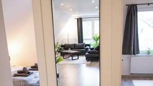 Un interior moderno con un espejo grande, suelo de madera, una cama, un sofá y una zona de comedor.