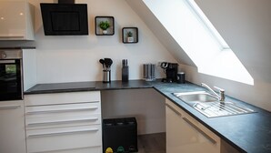 Una cocina moderna con horno integrado, extractor de aire negro, pileta de acero inoxidable y encimera negra. Hay dos plantas en macetas en la pared y una cafetera en la encimera.