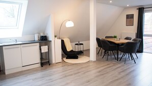 Una cocina moderna con armarios blancos, una zona de comedor con una mesa de madera y sillas negras, y una silla negra con una toalla amarilla.