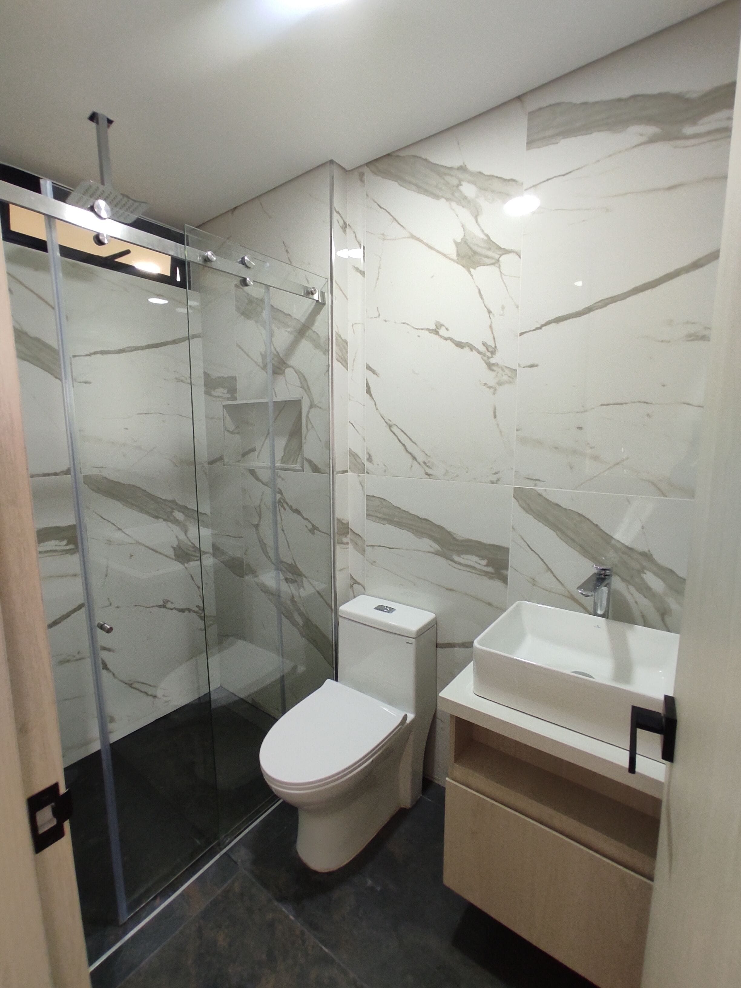 Un baño moderno con cabina de ducha de vidrio, inodoro y lavabo.