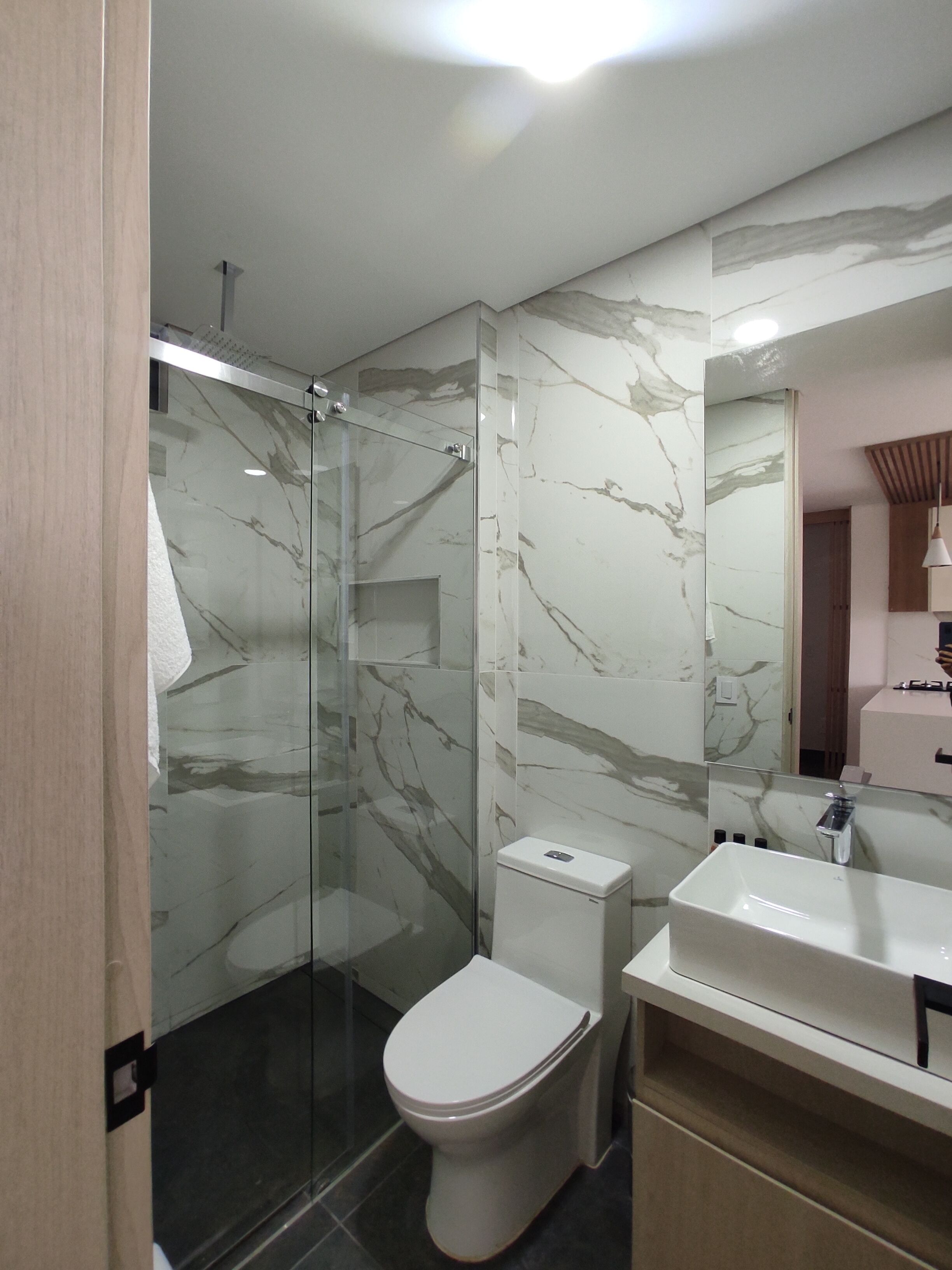 A modern bathroom with a glass shower enclosure, a white toilet, and a vanity with a mirror.