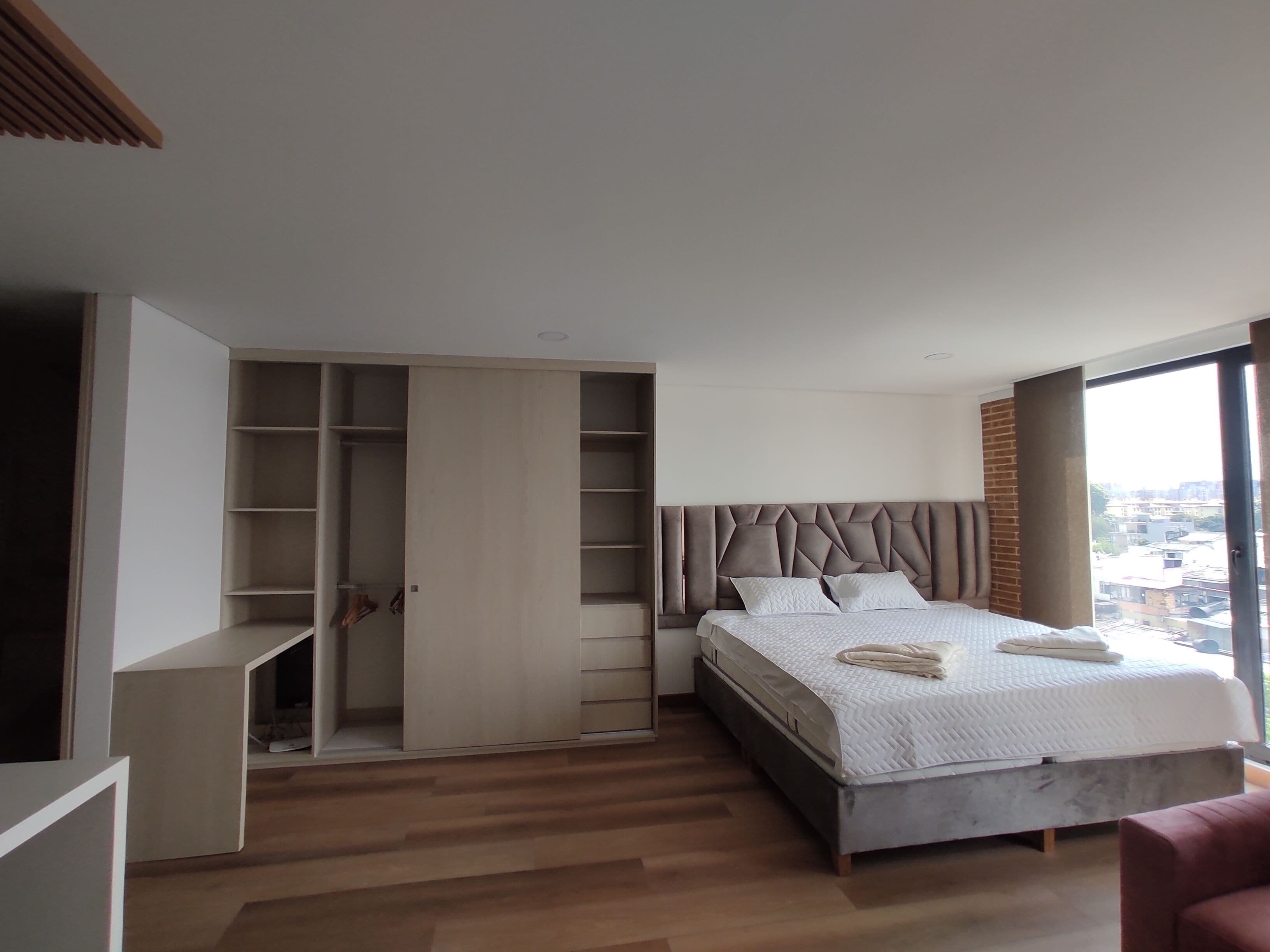 A bedroom with a large bed, a wardrobe, and a view of the city.