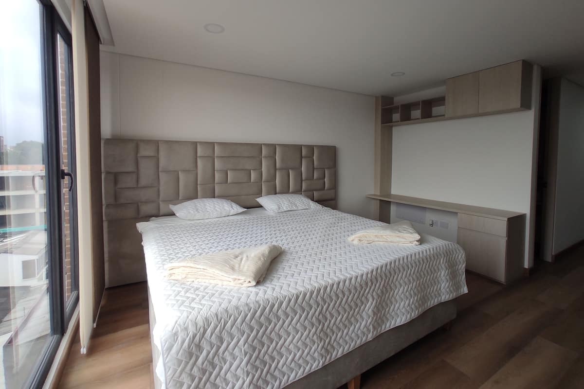 Quarto moderno com uma cama grande, cabeceira e espaço de armazenamento embutido.
