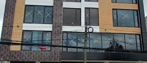 Un edificio de varios pisos con diseño arquitectónico moderno, que presenta grandes ventanales y una combinación de paneles de fachada beige y oscuros.