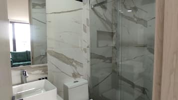 A modern bathroom with a glass-enclosed shower, a white sink, and a toilet.