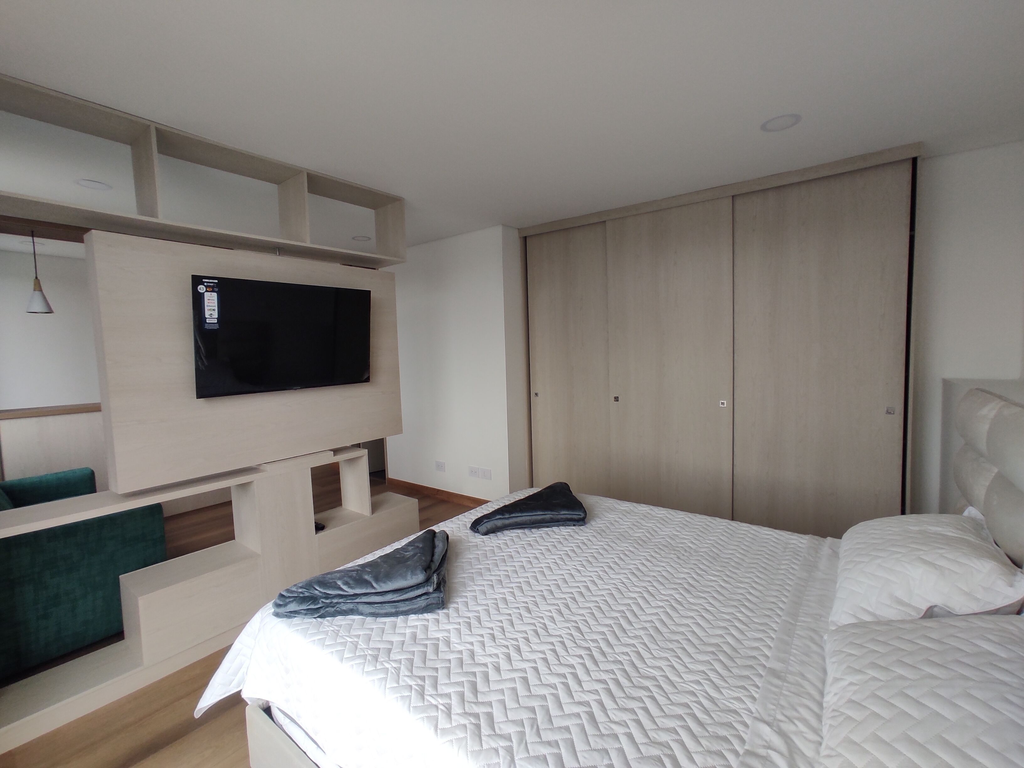 A bedroom with a bed, a TV mounted on a wall, and a wardrobe.