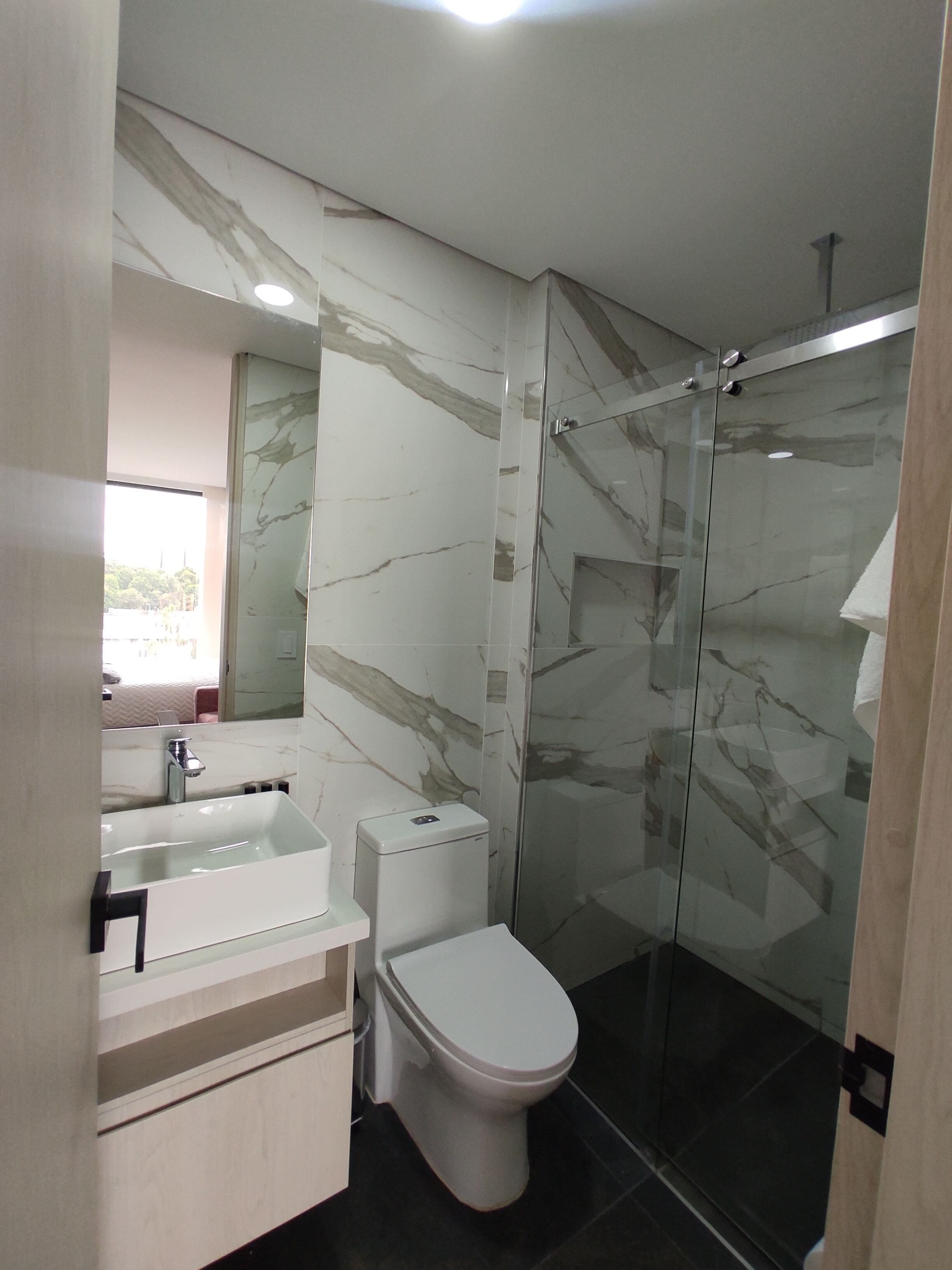 A modern bathroom with a glass shower enclosure, a marble backsplash, and a white sink.