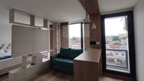 A modern living room with a green sofa, wooden accents, and a large window offering a city view. - Modelia Living & Parking (Bogotá)