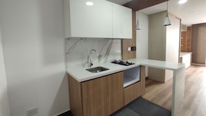 A modern kitchen with a marble countertop, wooden cabinets, a stainless steel sink, and a built-in gas stove. - Modelia Living & Parking (Bogotá)