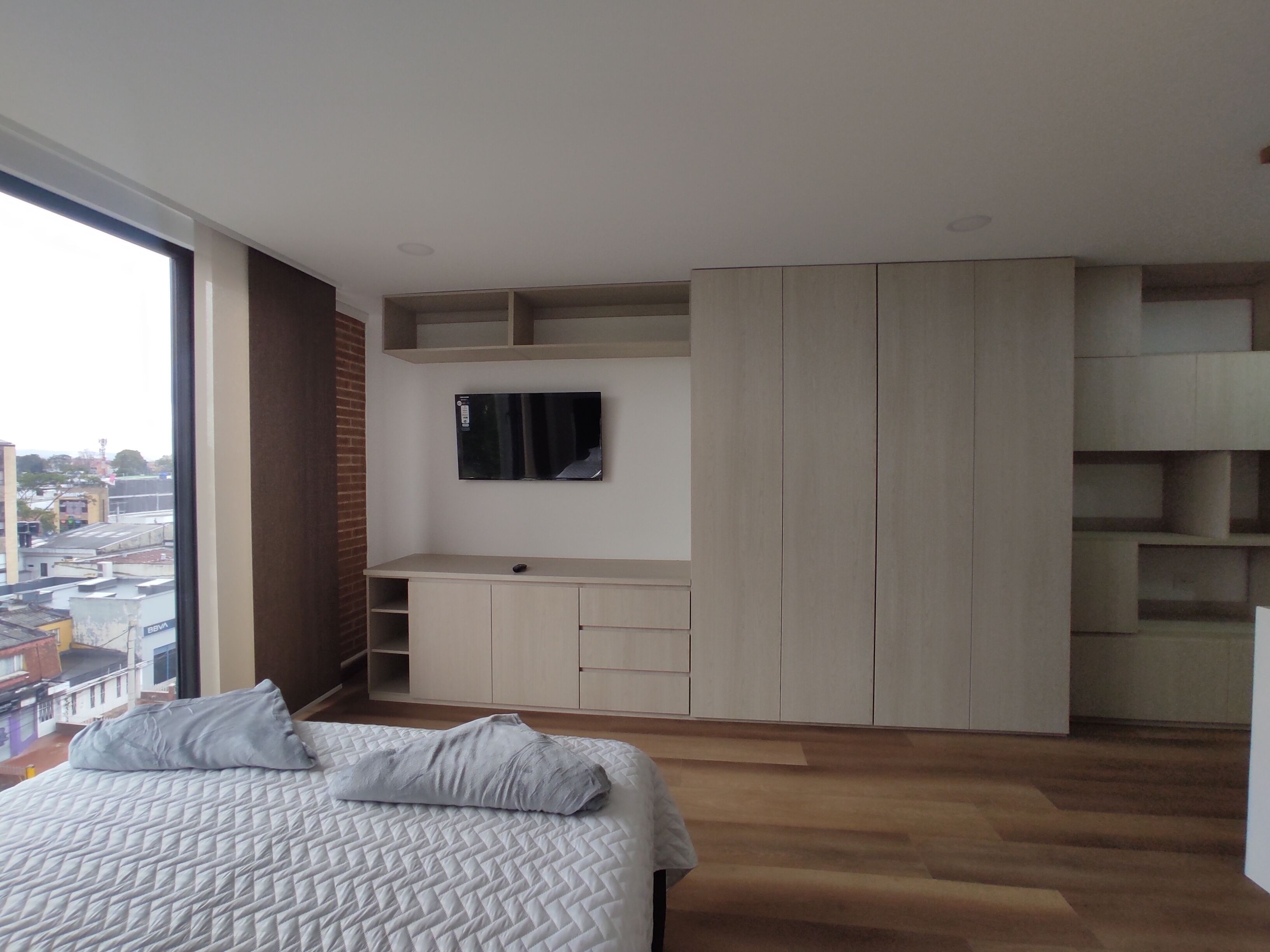Une chambre à coucher comprenant un lit, un téléviseur fixé au mur et des rangements intégrés.