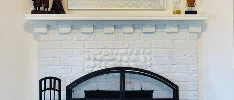 A room with a white brick fireplace, a black metal screen door, and a mirror above the fireplace.