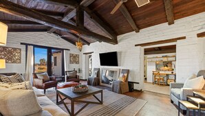 Un vaste salon doté d’un haut plafond, de poutres apparentes en bois, d’un grand téléviseur fixé au mur et d’un coin salon confortable avec un canapé et des fauteuils.