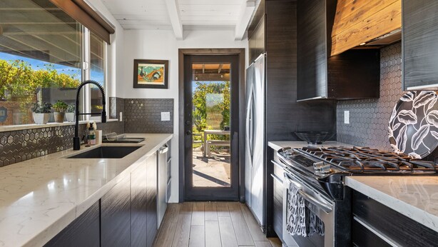 Une cuisine moderne dotée d’un grand îlot central, d’appareils électroménagers en acier inoxydable et donnant sur un patio extérieur.