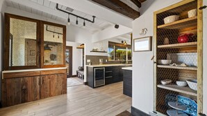 Une cuisine moderne avec des armoires en bois, un îlot central intégré et une étagère métallique où sont rangés la vaisselle.