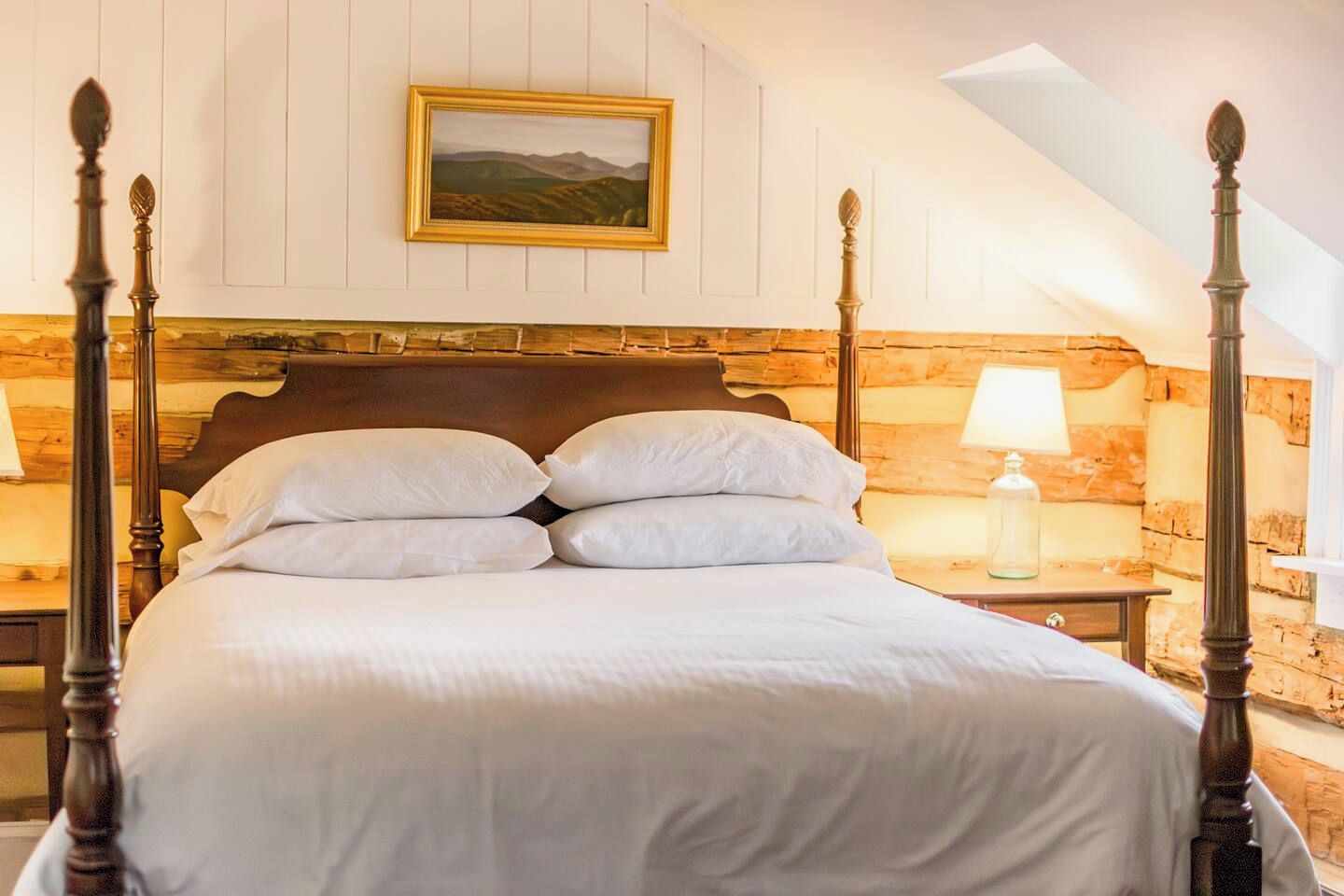 Un lit à baldaquin avec une literie blanche, une tête de lit en bois et une table de chevet avec une lampe.
