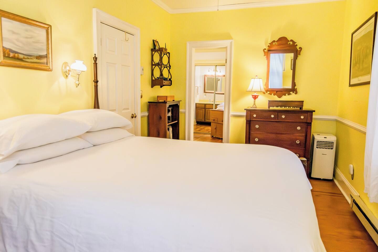 Une chambre à coucher avec un grand lit, une commode, un miroir et une porte donnant sur une autre pièce.