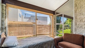 A room with a bed, a brown sofa, and large windows with a view of a garden and a house. - Sunlit Solace - Wanaka Holiday Home (Wanaka)