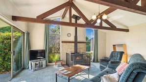 A cozy living room with a stone fireplace, a television, and a comfortable sofa. - Sunlit Solace - Wanaka Holiday Home (Wanaka)