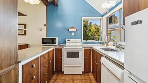A compact kitchen with wooden cabinets, a microwave, a stove, and a dishwasher. - Sunlit Solace - Wanaka Holiday Home (Wanaka)