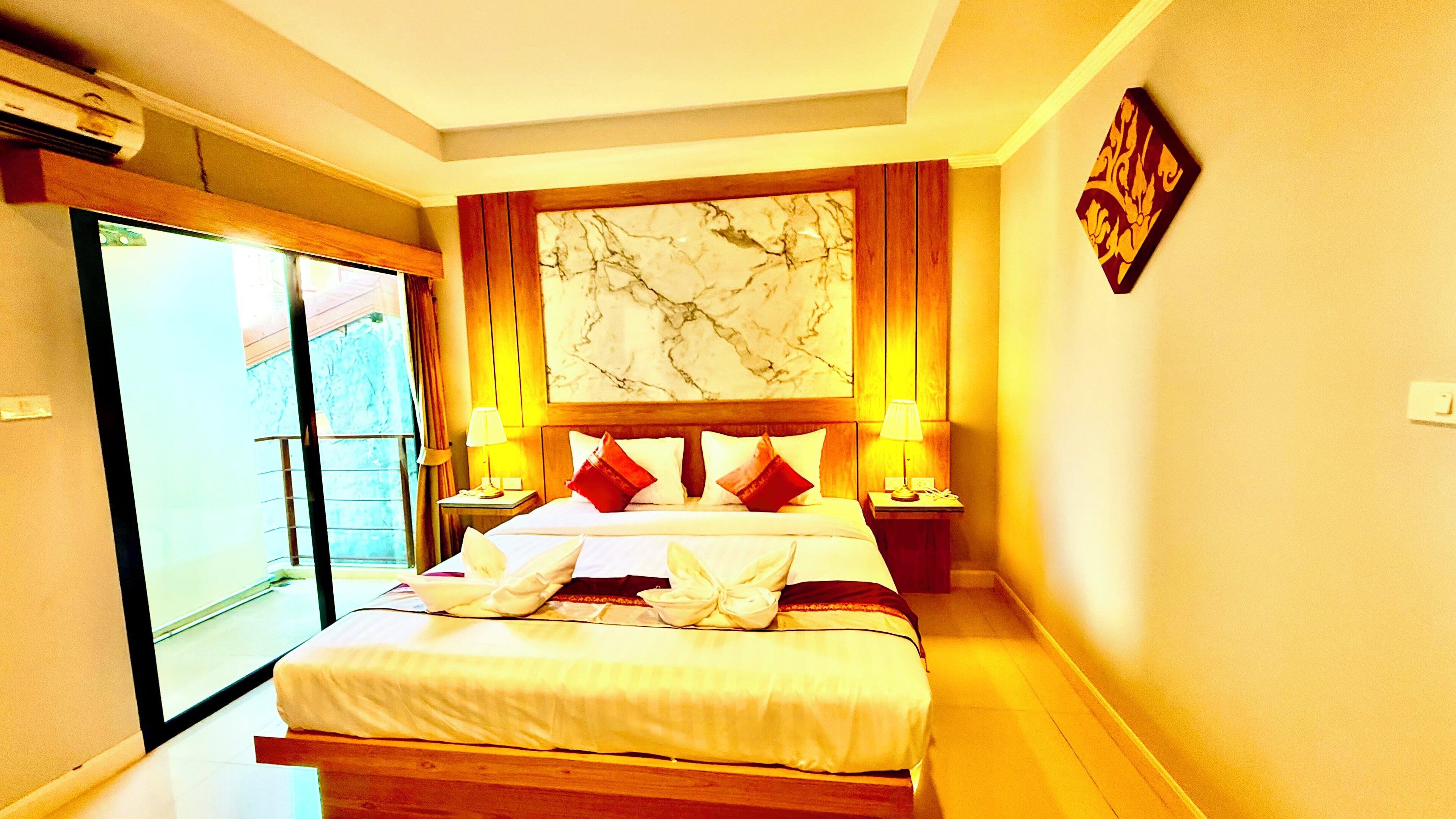 A hotel room with a large bed, two bedside lamps, a marble artwork above the bed, and a sliding glass door leading to a balcony.