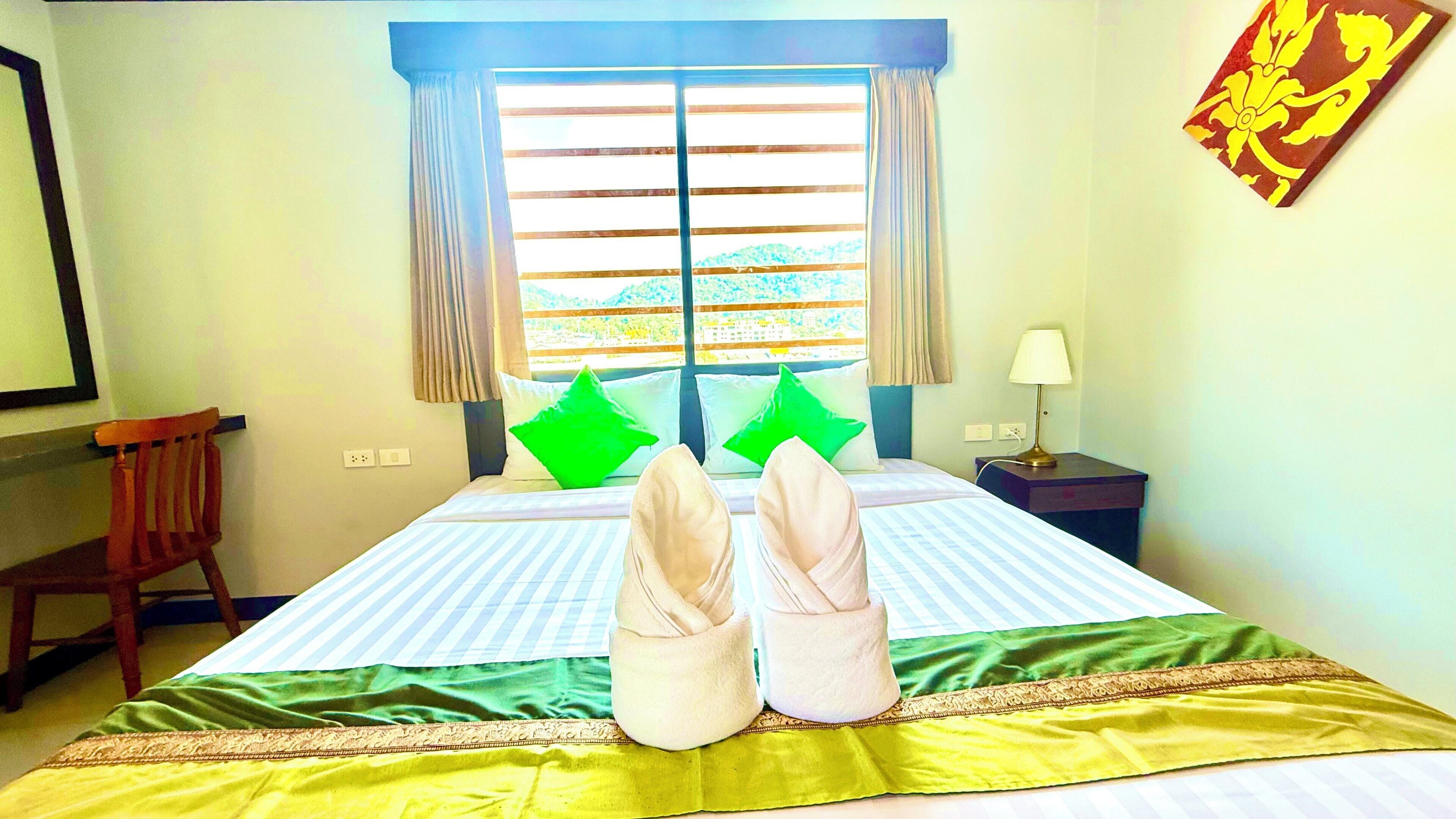 Un lit avec une couvre-lit à rayures, un oreiller vert et une paire de pantoufles blanches posées dessus.