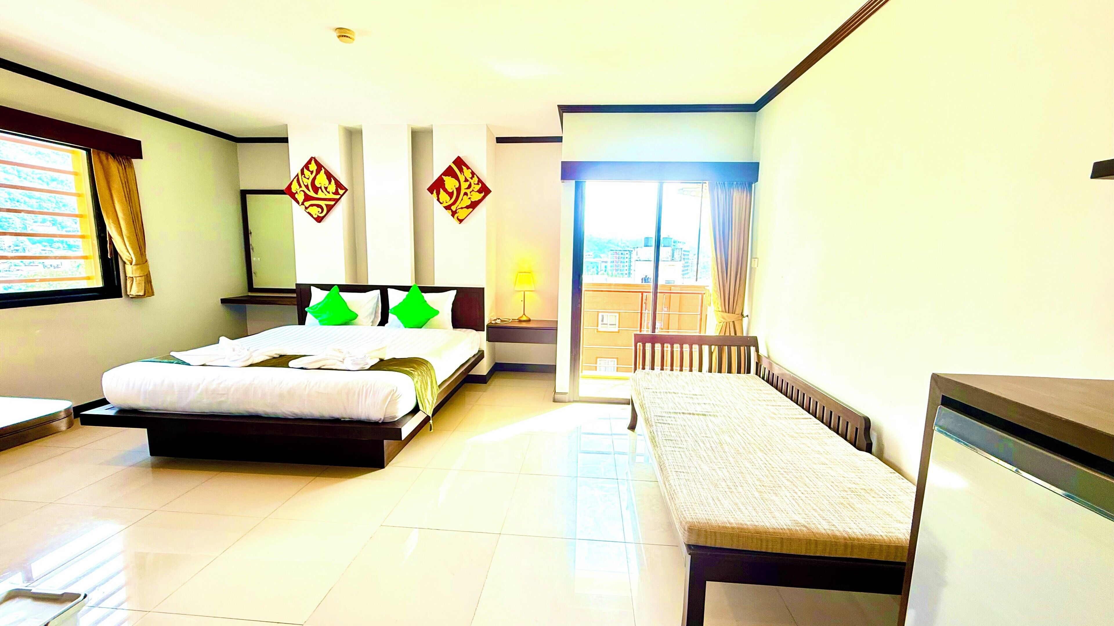 A hotel room with a bed, a bench, a desk, and a view of the city through the window.