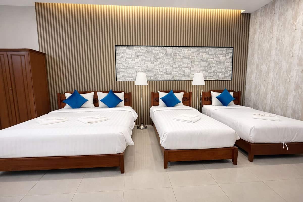 A hotel room with two single beds, a wooden wardrobe, a large framed cityscape artwork, and a tiled floor.