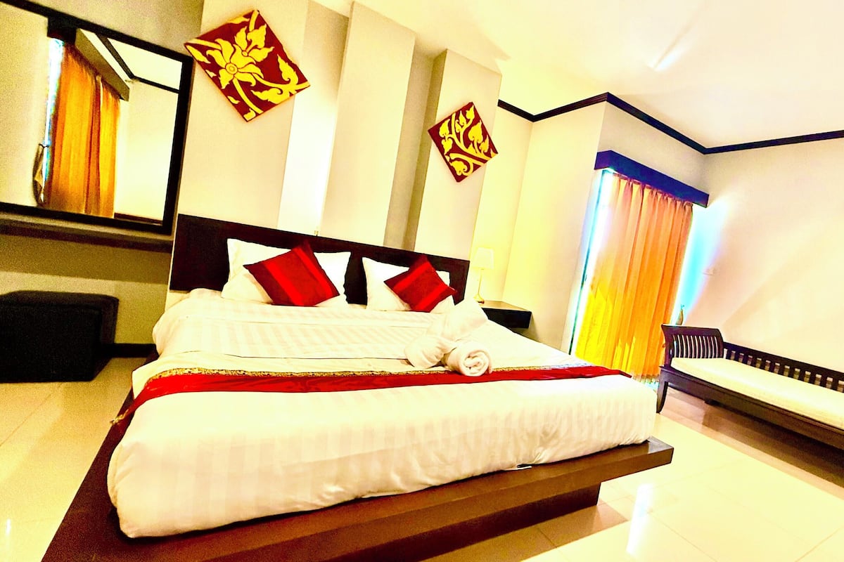 A modern hotel room with a large bed, a bedside table, a mirror, and a window with curtains.