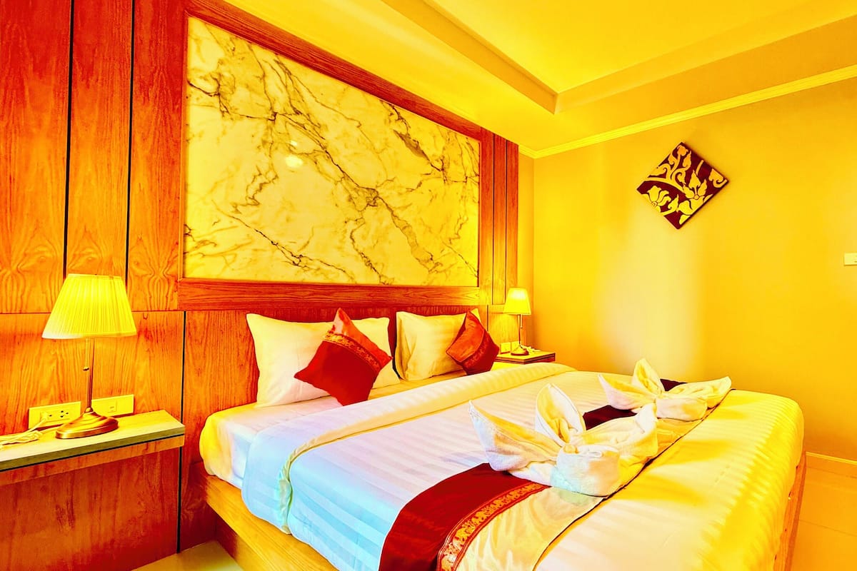 A hotel room with a large bed, wooden headboard, marble wall, and a painting.