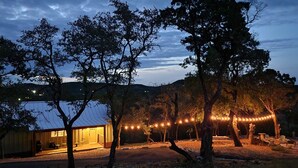A rustic cabin with a metal roof, surrounded by trees and a string of lights. - Stunning Views & Heated Cowboy Pool 5 min to River (Canyon Lake)
