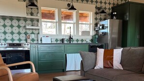 A compact kitchen with green cabinets, a black stove, and a dining area with a brown sofa and a wooden chair. - Stunning Views & Heated Cowboy Pool 5 min to River (Canyon Lake)