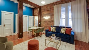 Een woonkamer met een blauwe wand, een bakstenen wand, een blauwe bank, een houten plafond en een eethoek met een tafel en stoelen.