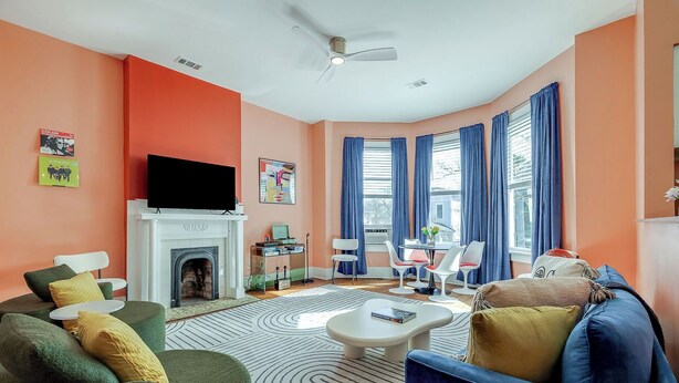 A living room with a fireplace, a television, and a dining area with blue curtains.