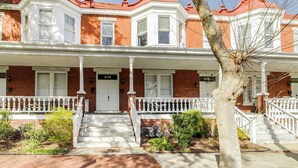 A two-story brick building with a red roof, white trim, and a front porch with white railings.