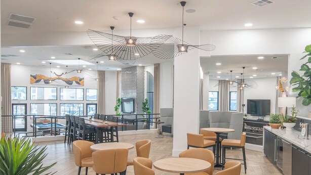 Un hall d’hôtel moderne doté de plusieurs espaces de détente, notamment des tables et des chaises rondes, un grand écran de télévision et une variété de plantes.