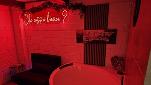 Et værelse med et stort badekar, en lille sofa og et neonskilt.