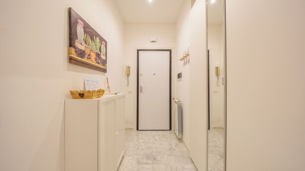 A hallway with a marble floor, a door at the end, a painting on the wall, and a wooden object on a counter. - Cozy Flat near Vatican and Metro Station (Roma)
