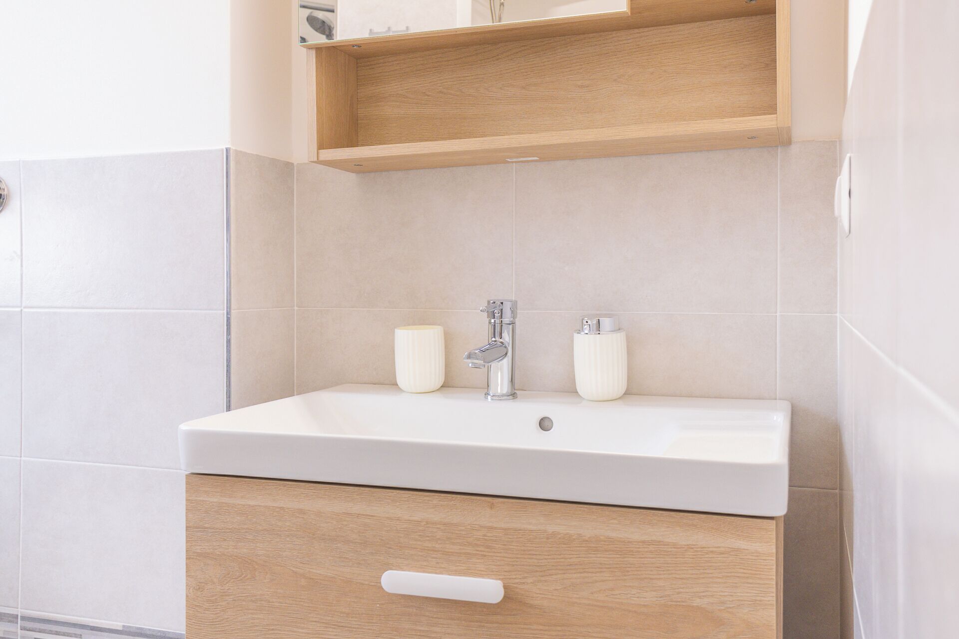 A bathroom with a white sink, two white candles, and a wooden shelf above the sink.