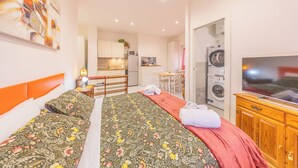 A bedroom with a bed, a desk, a chair, a TV, a washing machine, and a kitchen area. - Cozy Flat near Vatican and Metro Station (Roma)