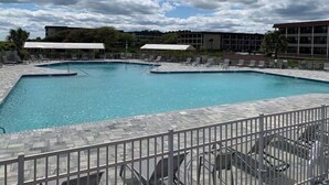 Una piscina con bordo piastrellato e poltrone da relax, circondata da una recinzione.