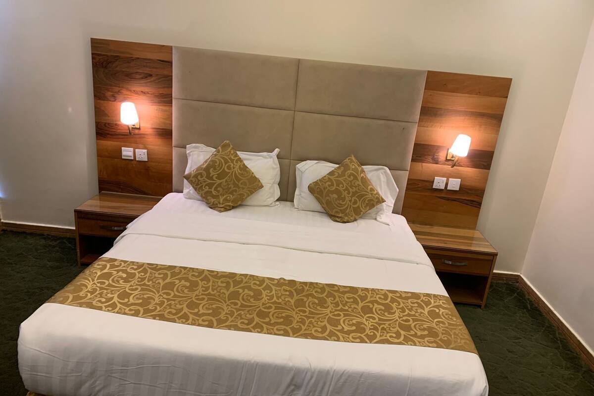 Un lit bien fait, recouvert d’une couvre-lit à motifs, agrémenté de deux coussins décoratifs et doté d’une tête de lit avec des lampes fixées au mur.