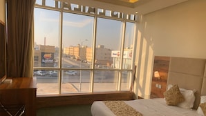 Una habitación de hotel con un ventanal grande, una cama con cubrecama estampado, un escritorio y una silla.