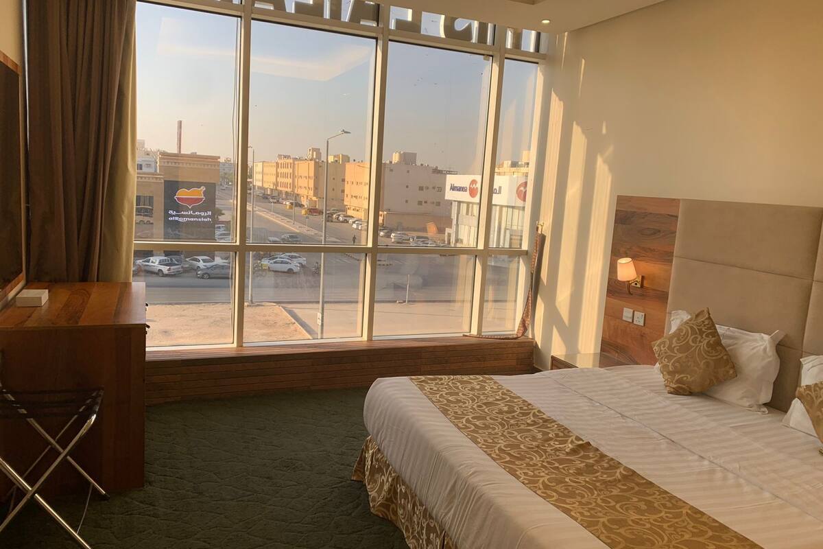 Une chambre d’hôtel avec une grande fenêtre, un lit recouvert d’une courtepointe à motifs, un bureau et une chaise.