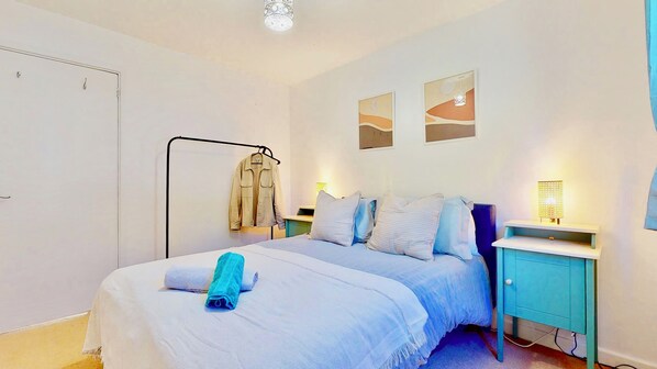 A bedroom with a bed, two bedside tables, a wardrobe, and a clothing rack.