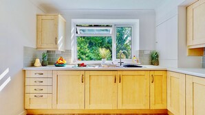 A kitchen with wooden cabinets, a window with a view of greenery, and a fruit bowl on the counter.
