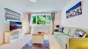 A modern living room with a TV, sofa, and a view of greenery through the window.