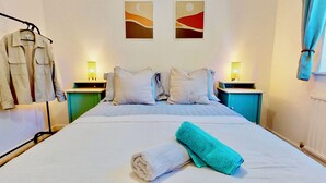 A neatly made bed with a white and teal towel, two nightstands with lamps, a green cabinet, and a wall with abstract art.
