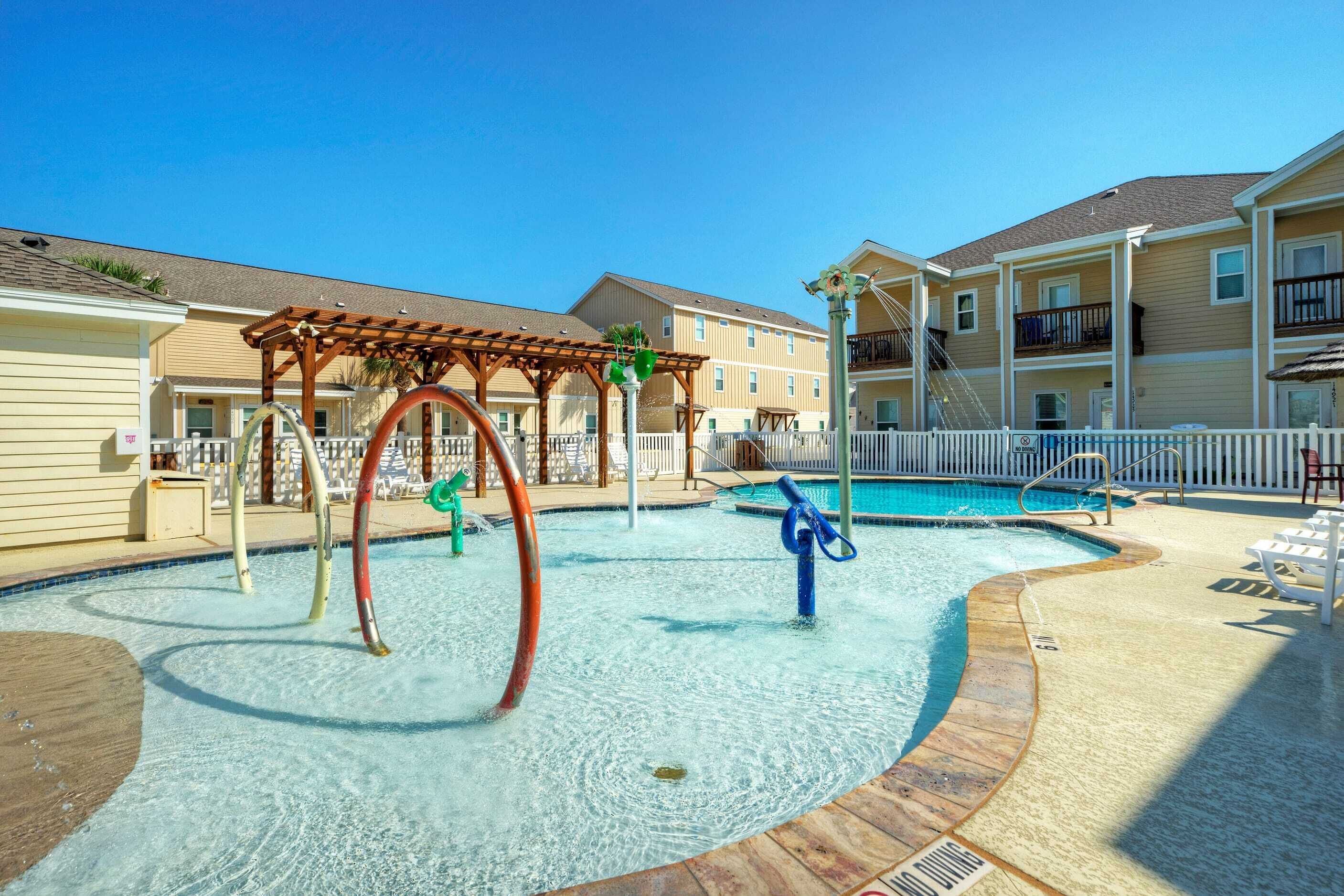 Un área de piscina con terraza de madera, pérgola y una pequeña fuente de agua.