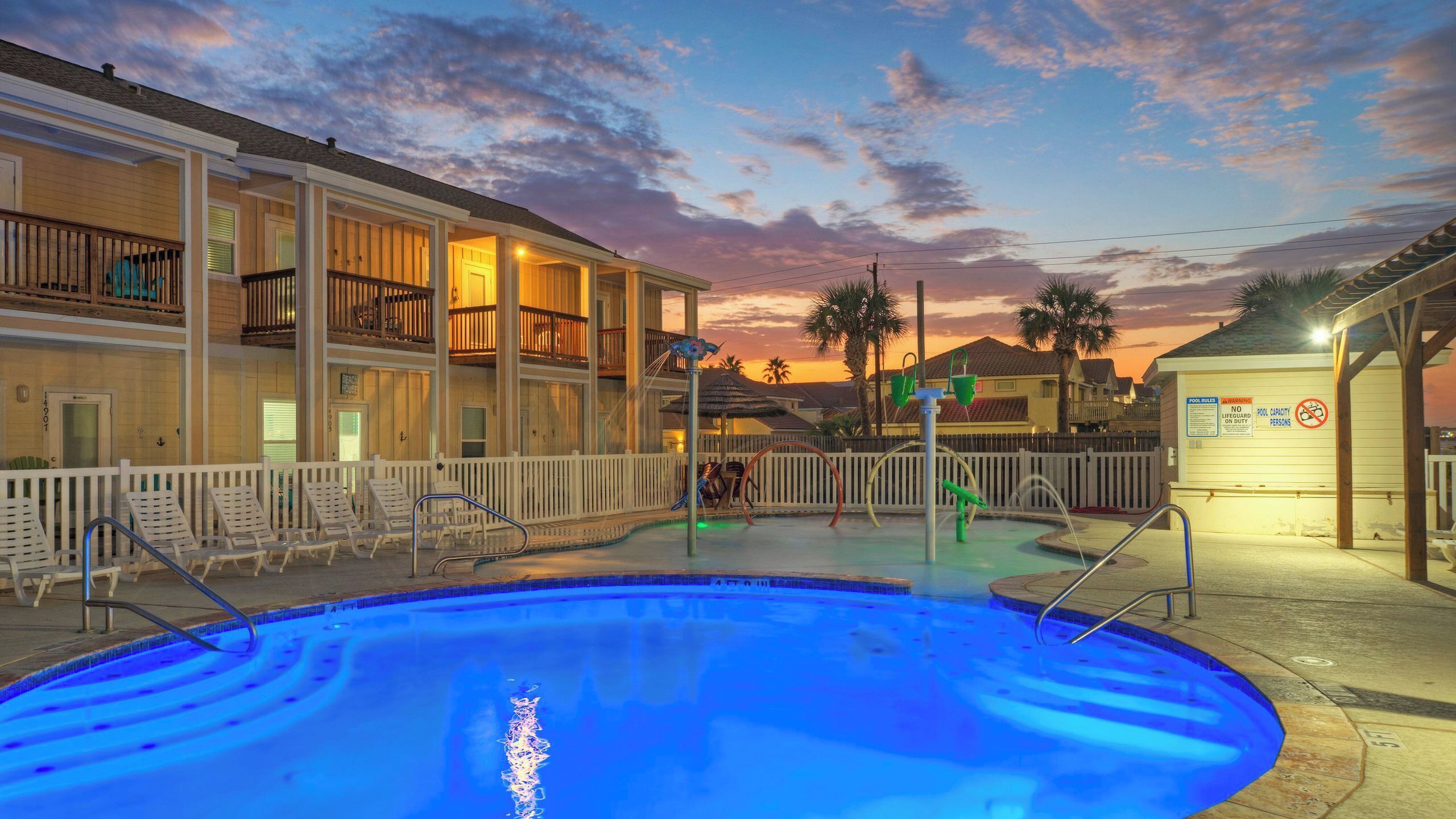 A swimming pool with lounge chairs, a wooden deck, and a building with balconies.